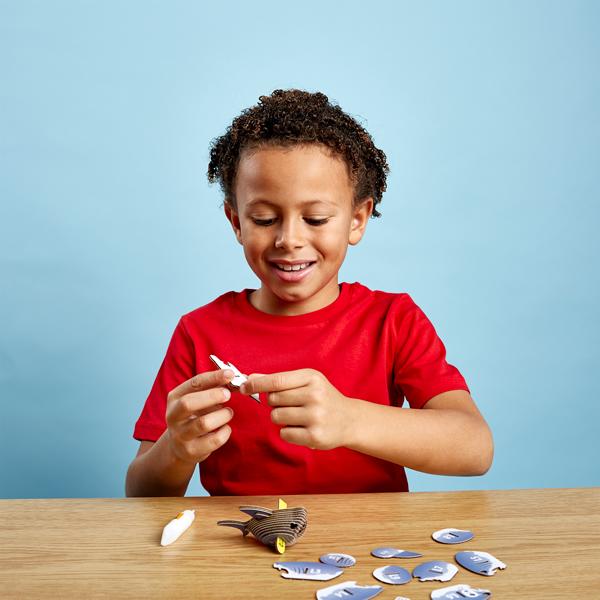 Young boy with dark curly hair and red tshirt sitting and putting the pieces of the eugy shark model together.