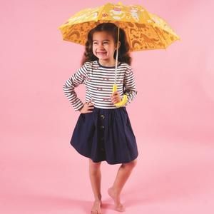 Young girl with dark hair, bare legs, navy skirt, striped top and holding a yellow umbrella. Pink background.