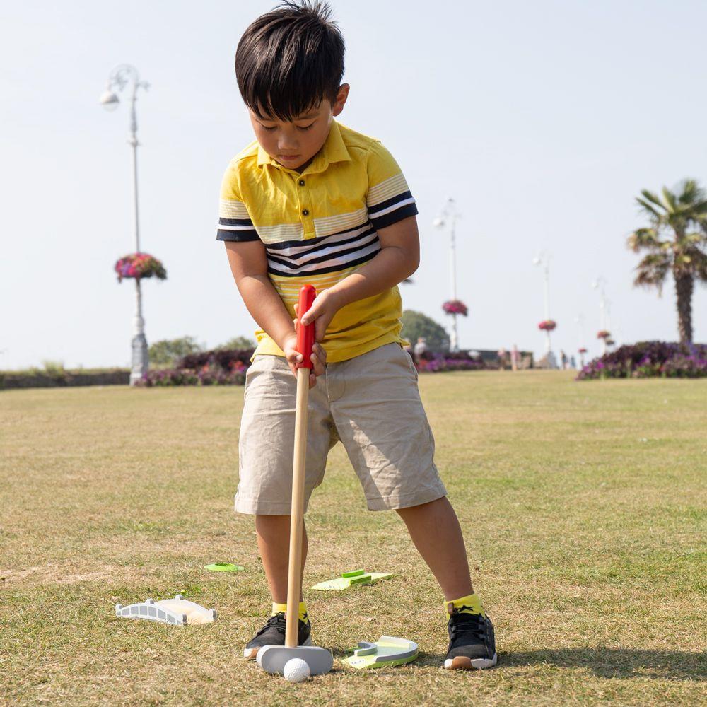 Young boy with dark hair and a yellow short-sleeved shirt with black stripes playing mini golf.