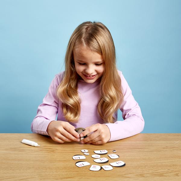 Girl with long blonde hair and long sleeved pink t-shirt sitting at a wooden table putting the panda model pieces together.