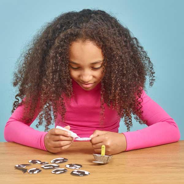 Girl with dark curly hair and long sleeve pink t shirt sitting putting peices of orca model together.