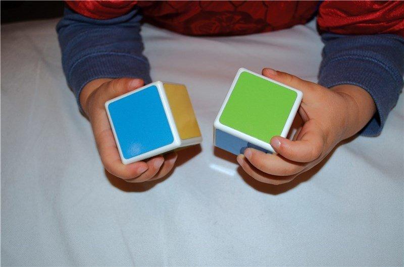 Child's hands playing with one green and one blue magnetic cubes.