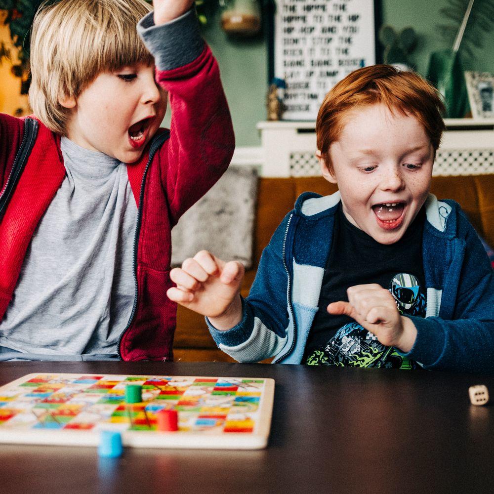 Two young boys cheering at the throw of the dice while playing snakes and ladders.