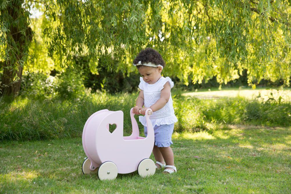 Young child pushing a pink Moover pram in a garden setting.