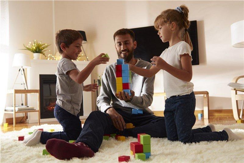 Man sitting with a boy on the left and girl on the right playing with colourful magnetic cubes.