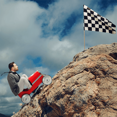 man driving a pedal car up a moutain to a chequered flag