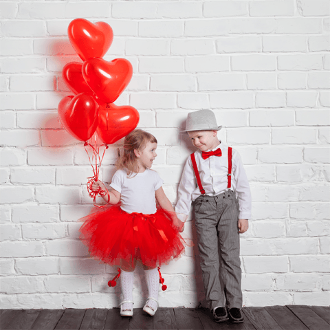 young boy and girl holding hands with red balloons