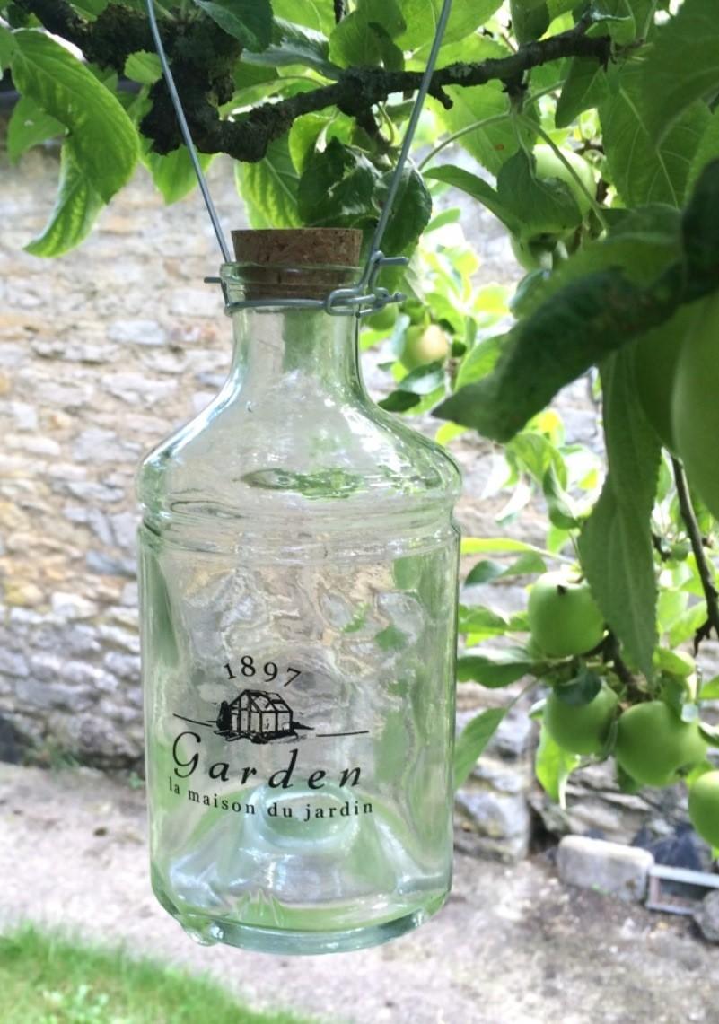 Clear glass bottle shaped wasp trap with words "1897  La Maison Du Jardin" on the front in white text.