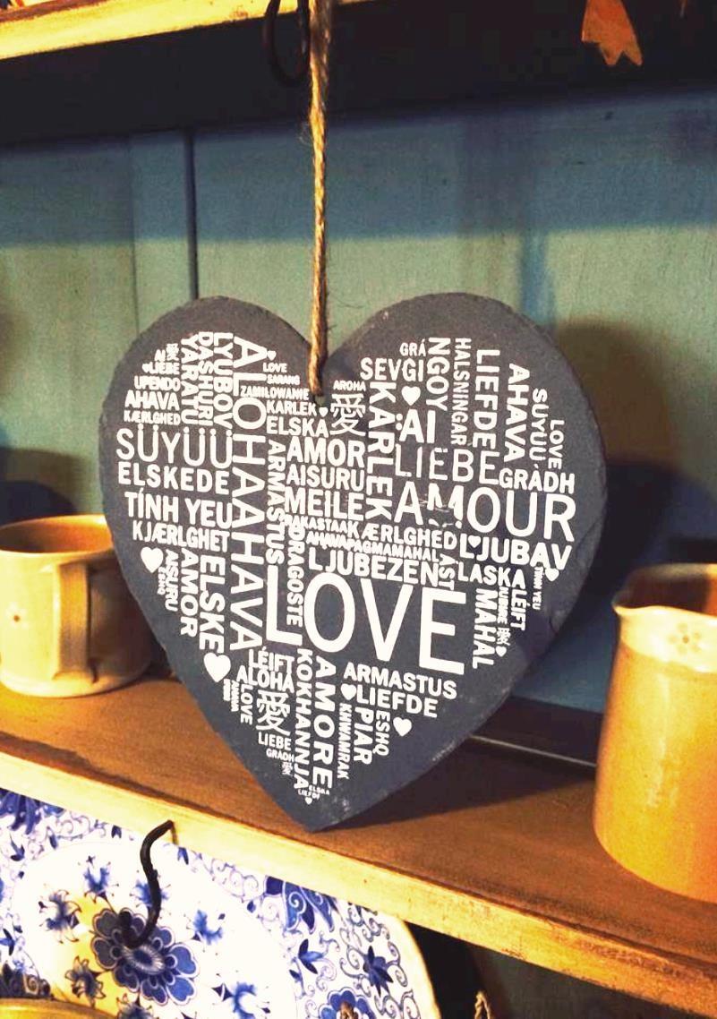 Heart shaped slate sign on twine hanger bearing the word for love in numerous languages all over it in various scripts both vertical & horizontal.
