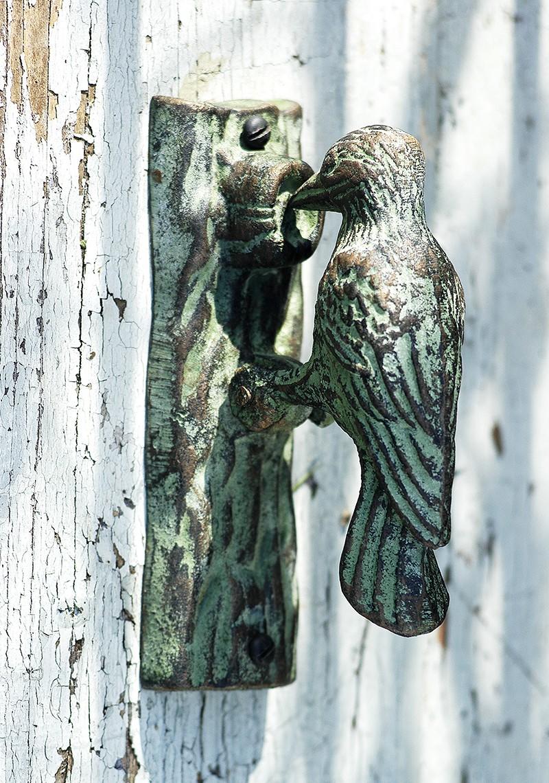 Antique style verdigris door knocker in the shape of a woodpecker fixed to a door.