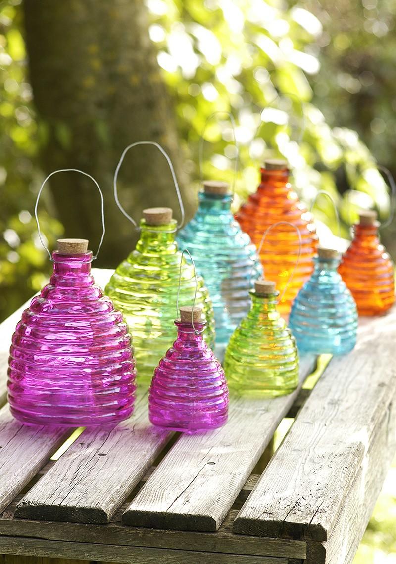 Colourful display of glass wasp traps in both small and large sizes on a garden table.