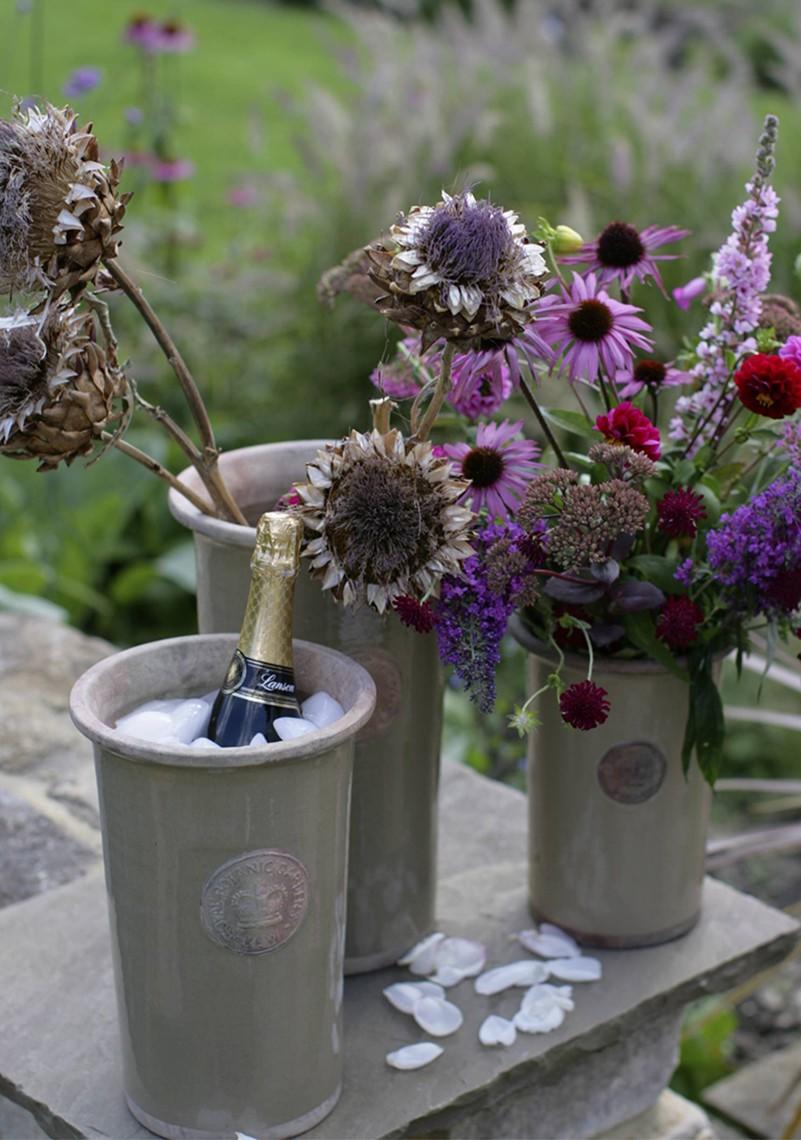 Range of Kew vases in Mocha colour on a garden table, two with flowers and one vase used as a wine cooler containing a bottle of champagne.