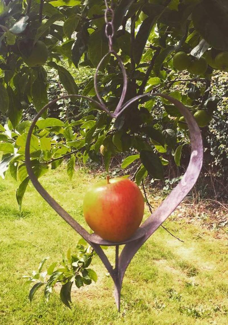 Heart shaped outline in metal with an upward facing spike at the bottom on which an apple is impaled for the birds to eat.