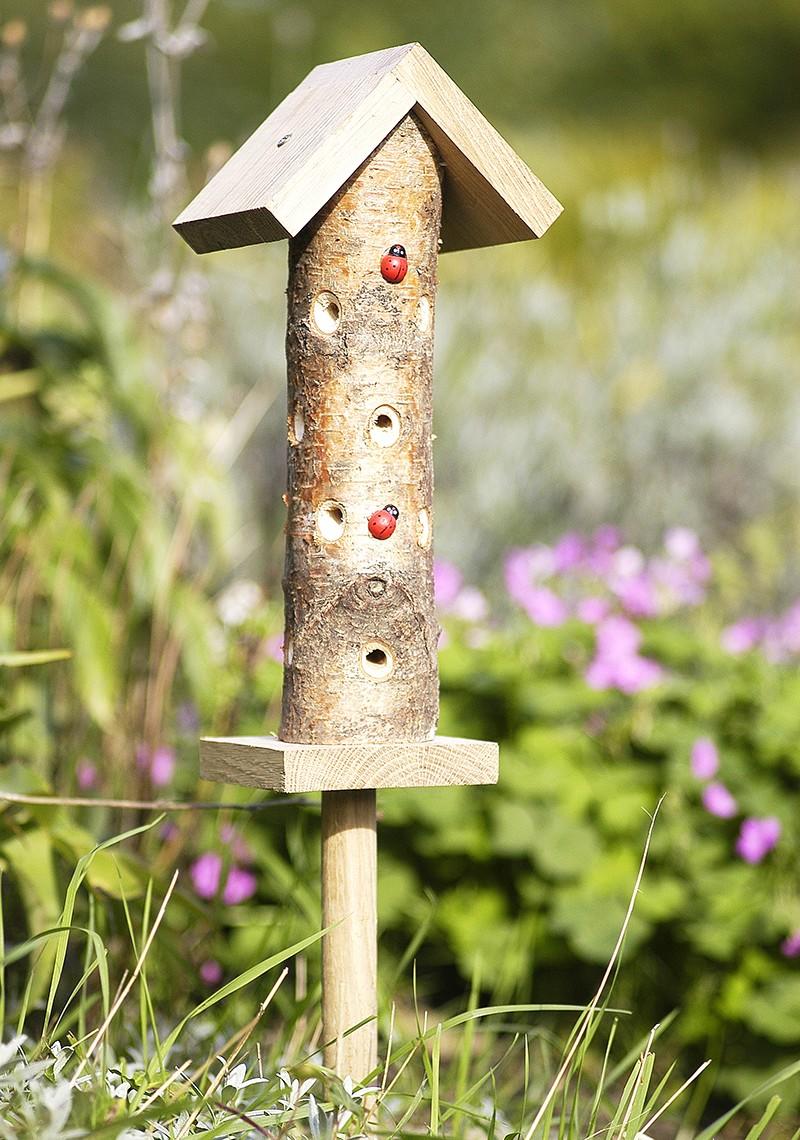 Upright, small, round log with holes for ladybirds and wooden roof on a pole stand