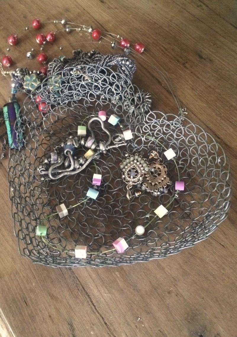 Wire heart shaped tray containing jewellery items on a wooden table