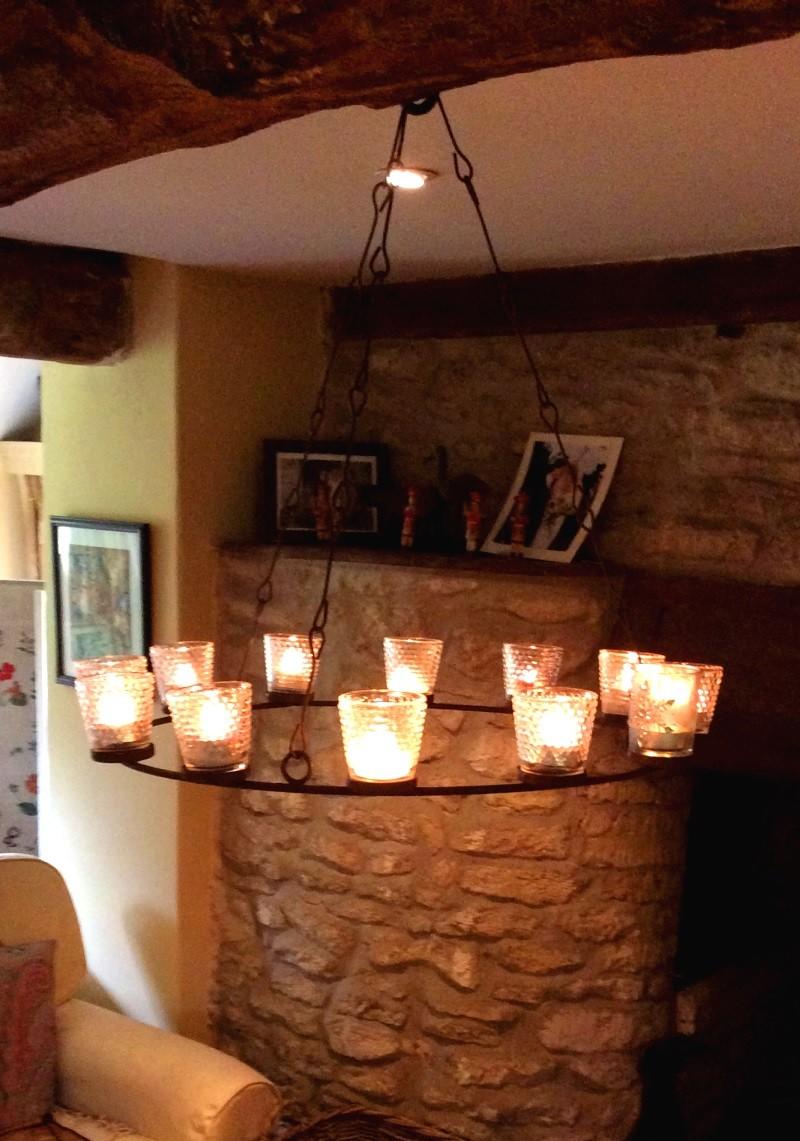 Glass votives on a circular metal support hanging from a wooden beam in a cottage.