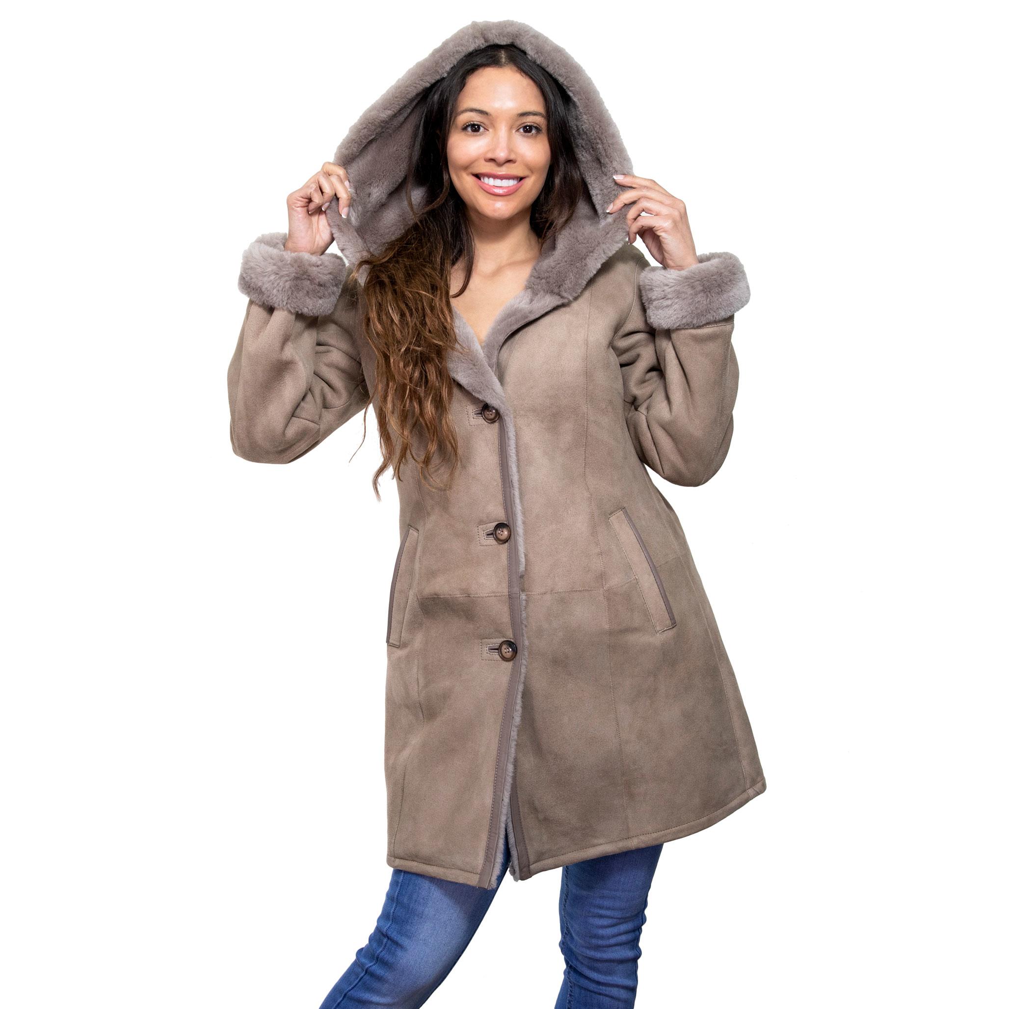 The model beams, as she cover her head with a hood. She is wearing a majestic sheepskin coat, with a suede finish in taupe. The interior is lined with soft opulent fur.