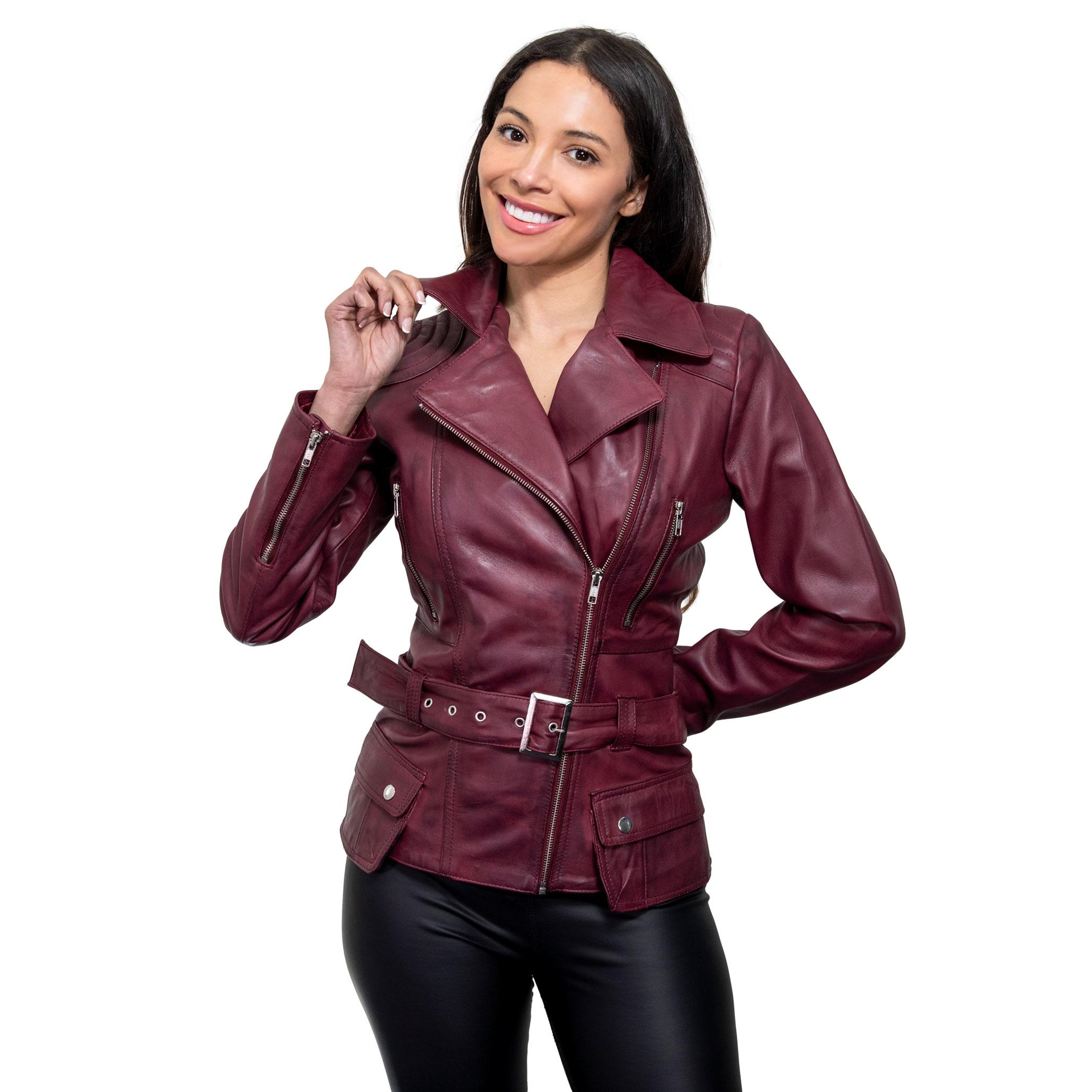 A female model smiles, wearing a long, premium leather jacket in a burgundy colour. The jacket features diagonal zips, small pockets, with a off centred front zip fastening, and a belted fastening.