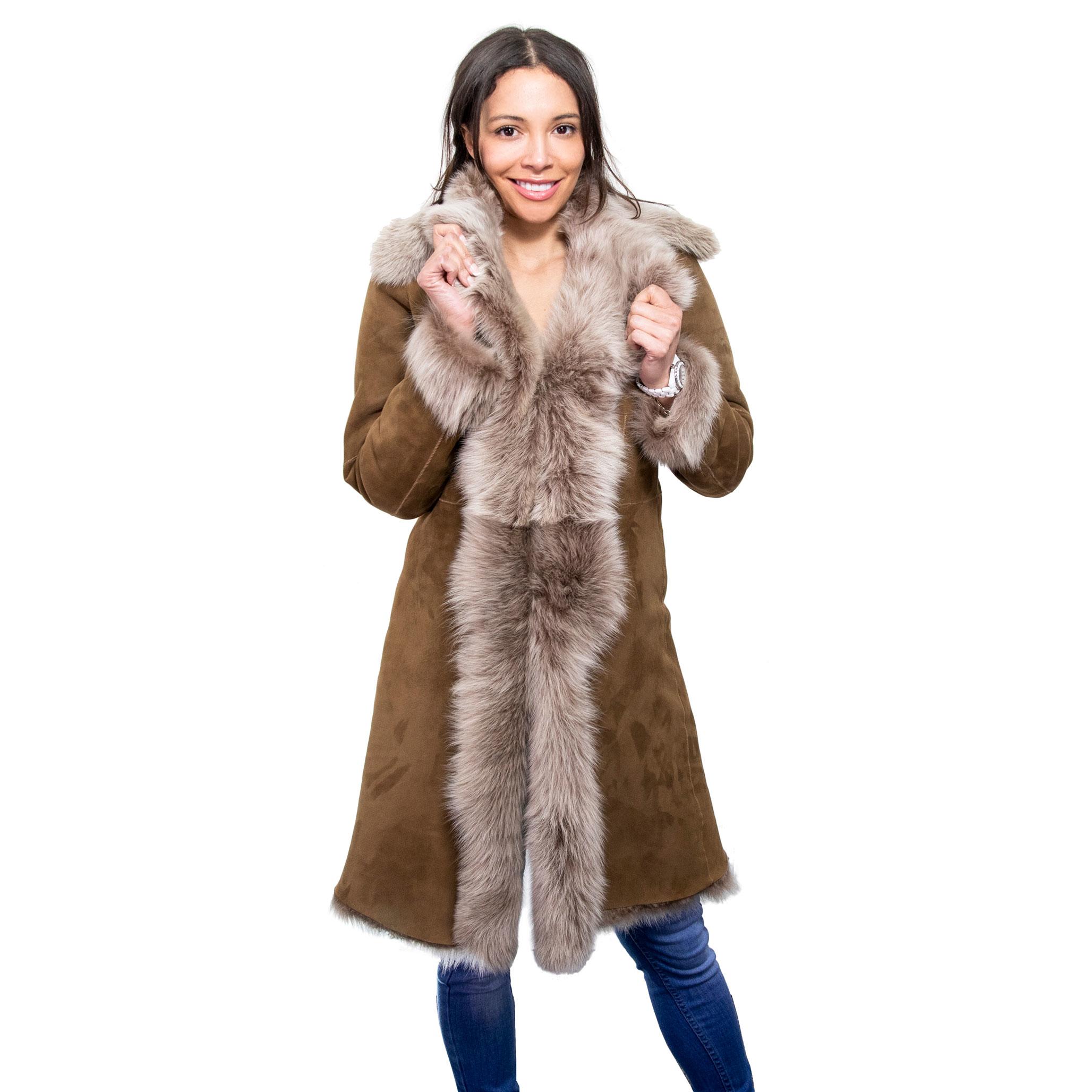 The female model feels the toscana fur, which drapes her long, tan sheepskin coat. The toscana fur colour appears grey, tan.
