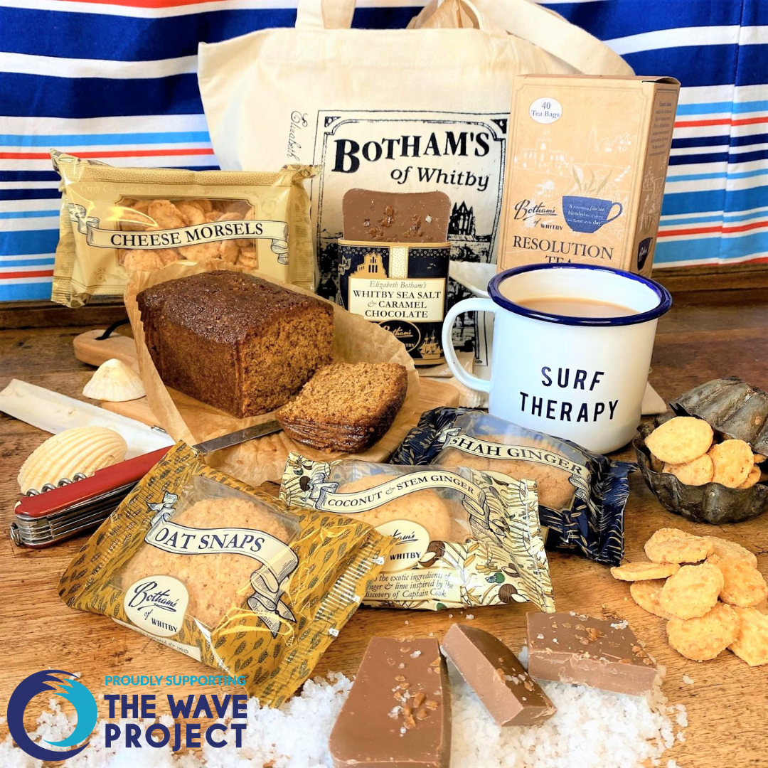 Image displays content of The WAVE Project charity hamper including: The WAVE Project Mug, Whitby Sea Salt & Caramel Chocolate Bar, Resolution Tea bags, Ginger Parkin, biscuits, Cheese Morsels and a Botham's long-handled Cotton Shopper.