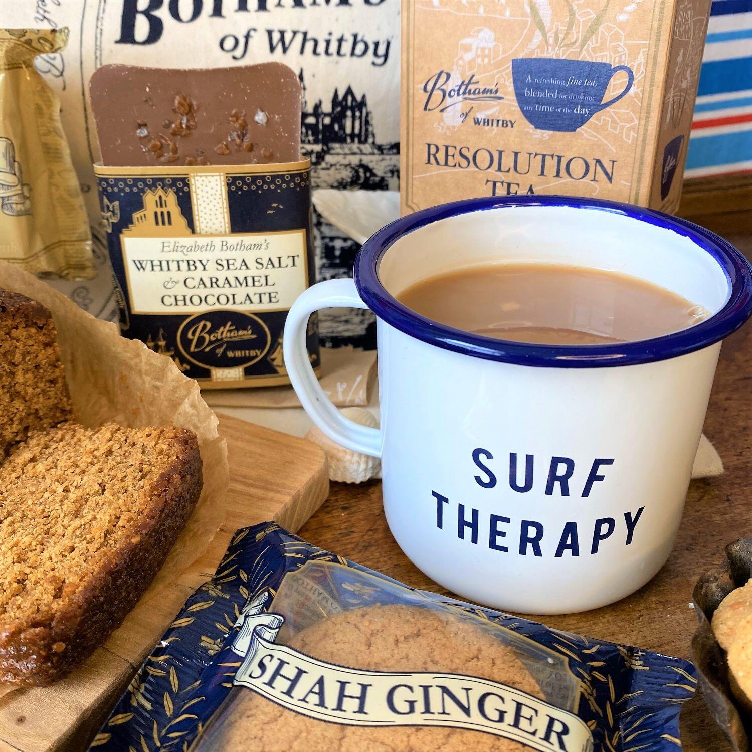 Close-up image of The WAVE Project Mug, which is white enamel with The WAVE Project text on one side and Surf Therapy on the other, all printed in inky navy blue.