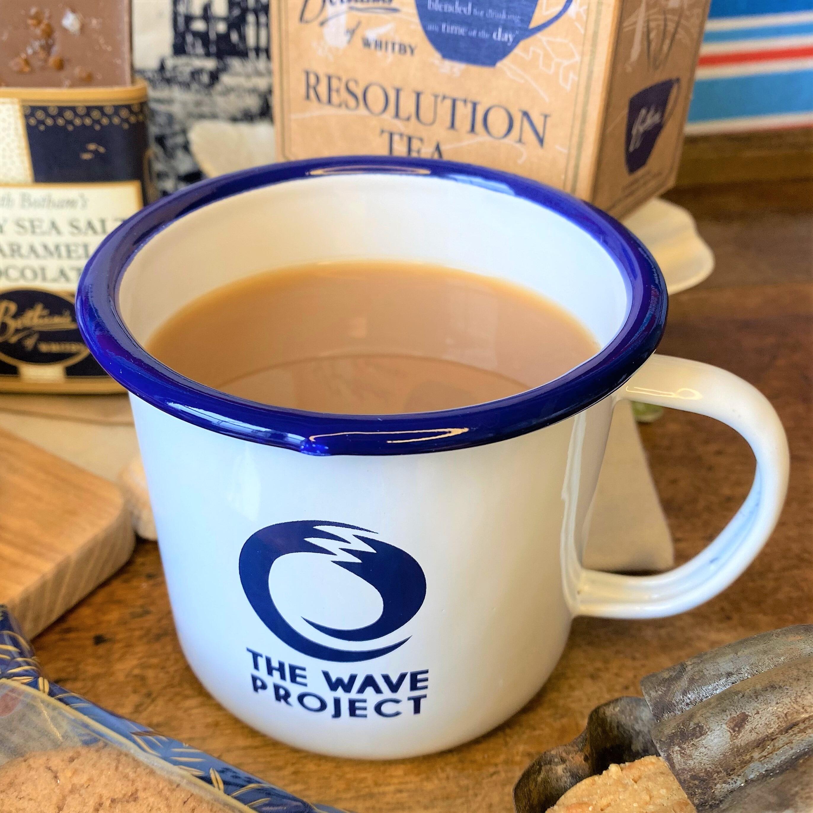 Close-up image of The WAVE Project mug containing strong tea and The WAVE Project logo printed on the white enamel mug.