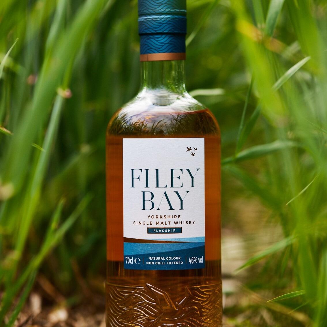 Hero shot of Filey Bay Whisky flagship in the barley field with lush green crops.