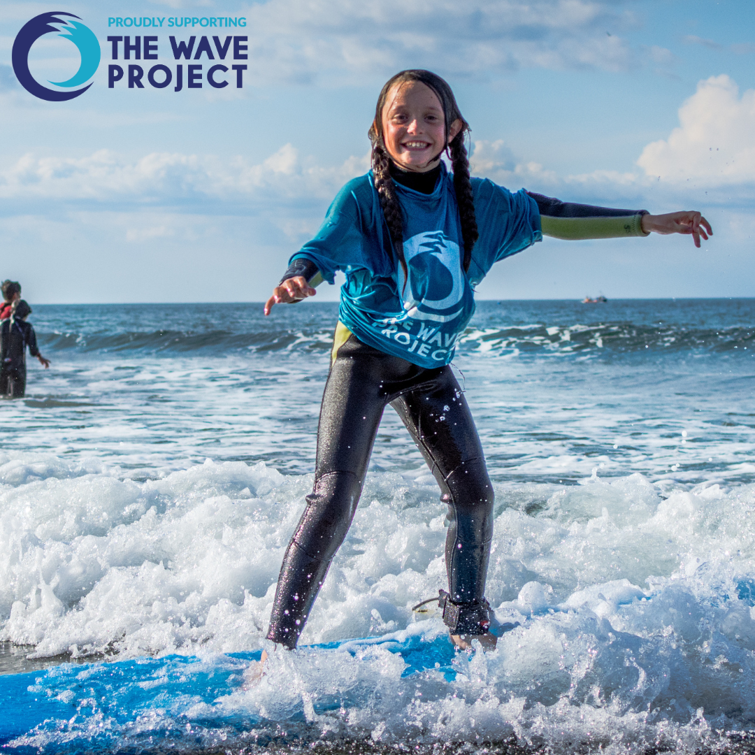 Image provided by The WAVE Project of female child riding a wave into the shore on a surf board - smiles galore!