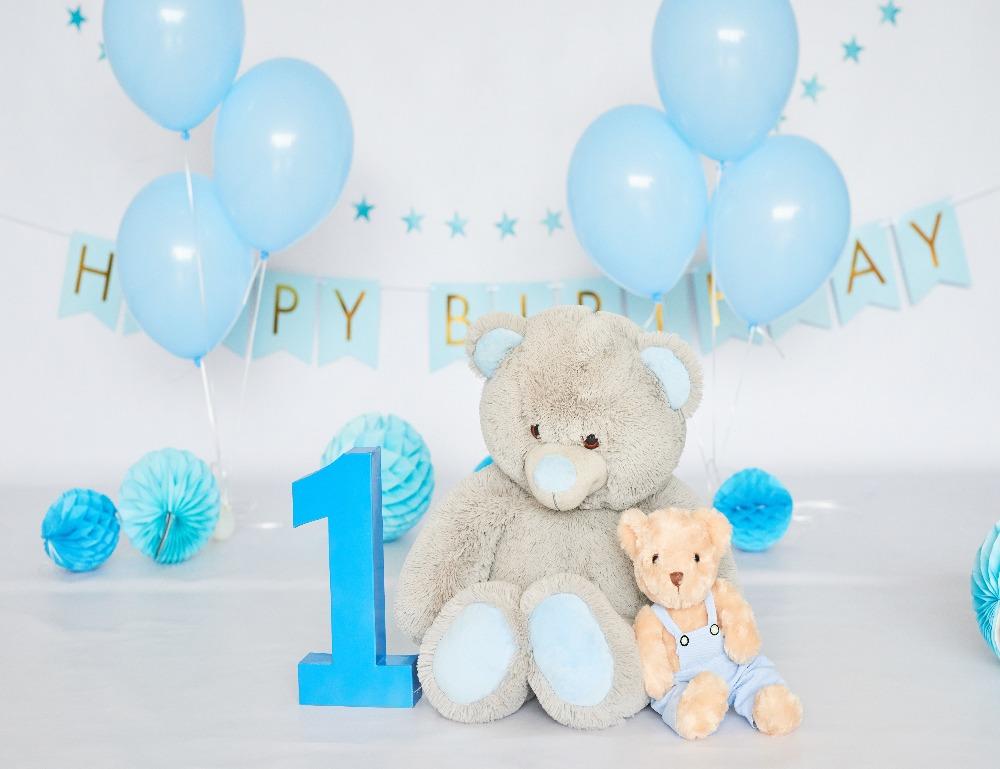 A boys 1st birthday setting with blue birthday banner, balloons and a number 1 sign with 2 teddy bears