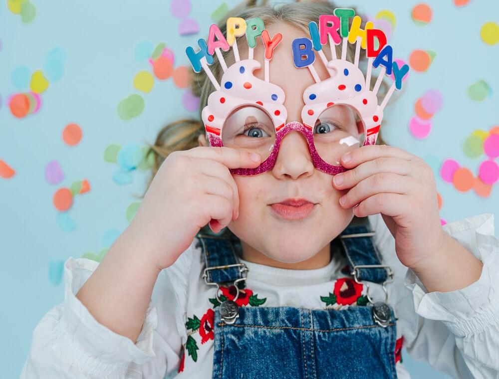 A cheeky little girl wearing Happy Birthday glasses