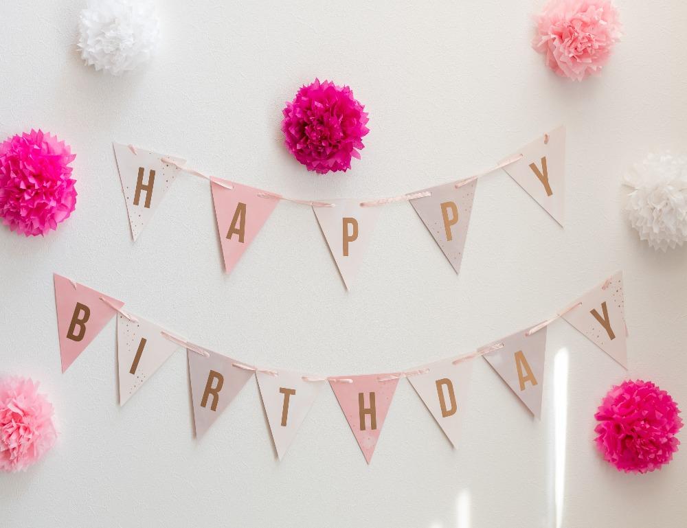 Pink Happy Birthday Bunting  with different shades of pink pom pom's attached to the wall.