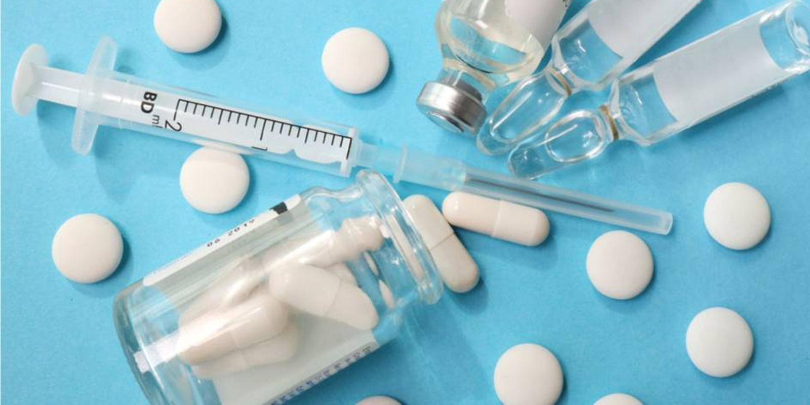Photo containing a syringe on a table with vials and capsules