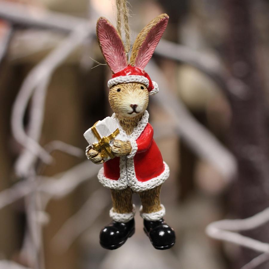 Standing tan colour rabbit with large upright ears wearing a Santa hat and suit, holding a Christmas present, hanging from jute string