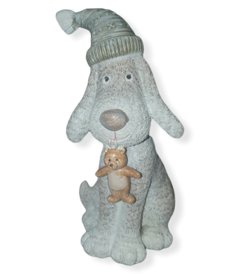 Beige and grey sparkly sitting dog, floppy ears and bobble hat, teddy bear hanging from its mouth.