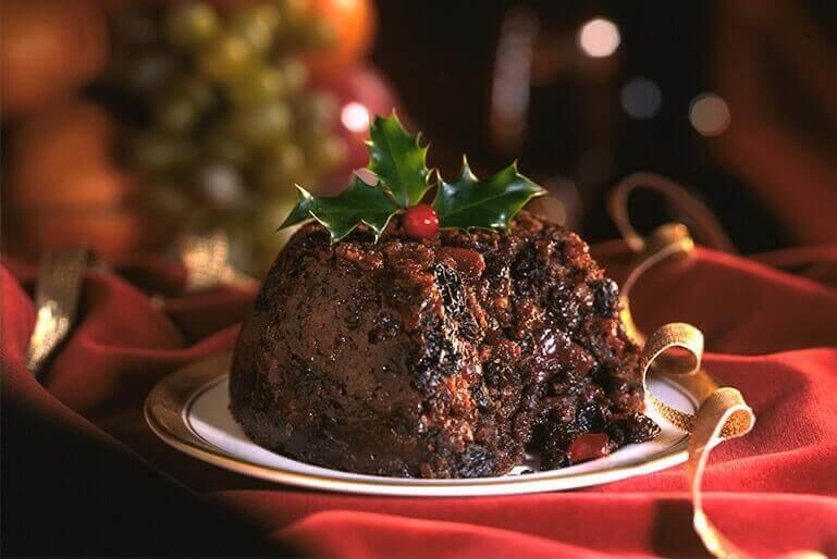 Christmas pudding, holly on top sitting on a white plate.