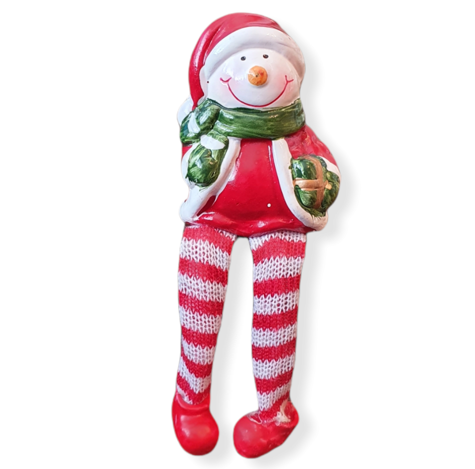 Ceramic sitting snowman wearing Santa outfit, green scarf big smile and orange nose. Green present in his hand. Red and white stripe cloth hanging legs and red ceramic boots.