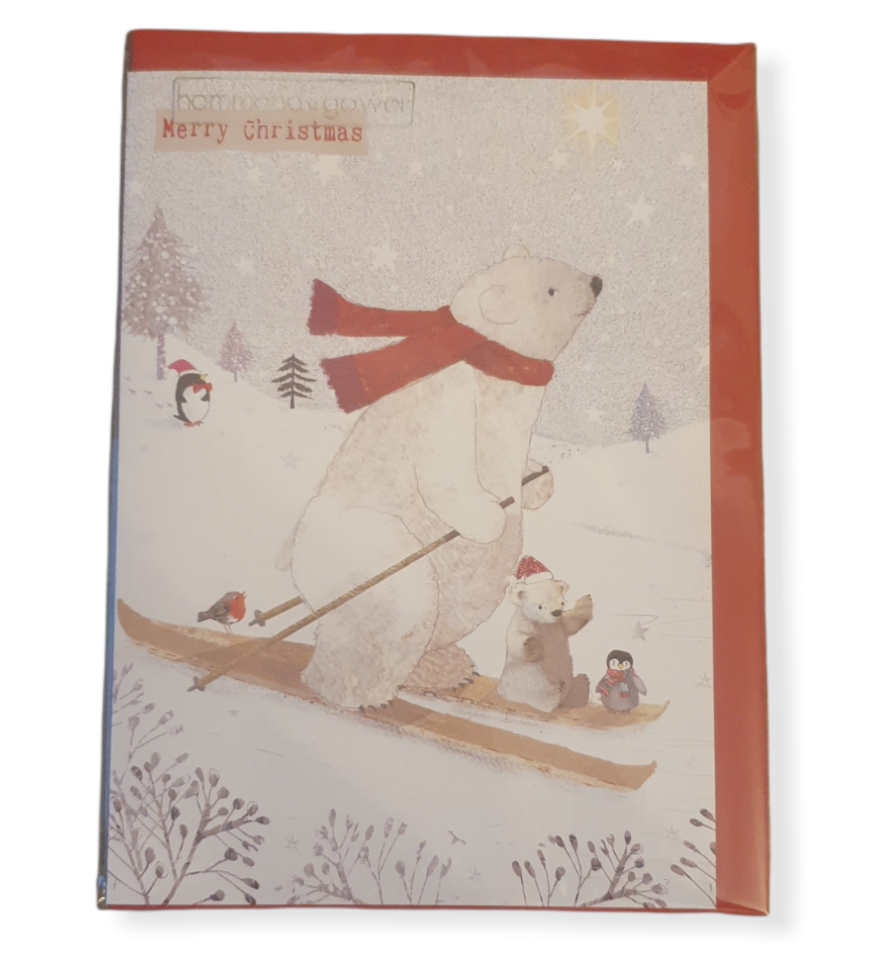 Snowy scene with trees and a penguin in the background, a large polar bear on ski's with a baby polar bear and a baby penguin sitting on the front of the Ski's