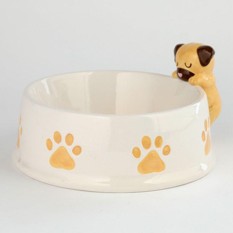 Cream ceramic circle bowl, tan colour paw prints all around edge and a tan pug with brown ears and muzzle with tiny pink heart for nose resting on the edge of bowl.