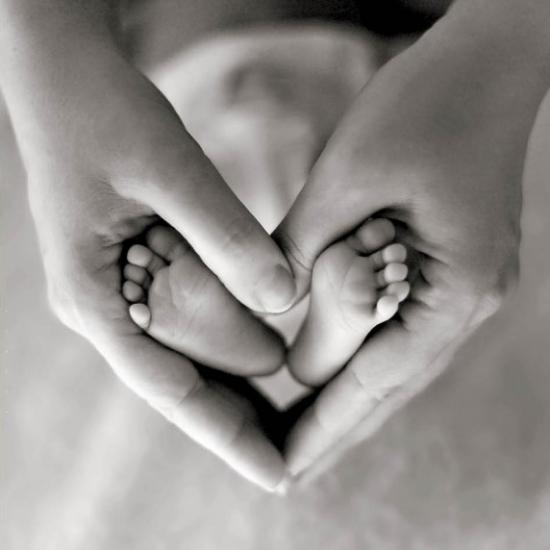 Black and White photo, adults hands in a heart shape around new baby's feet.