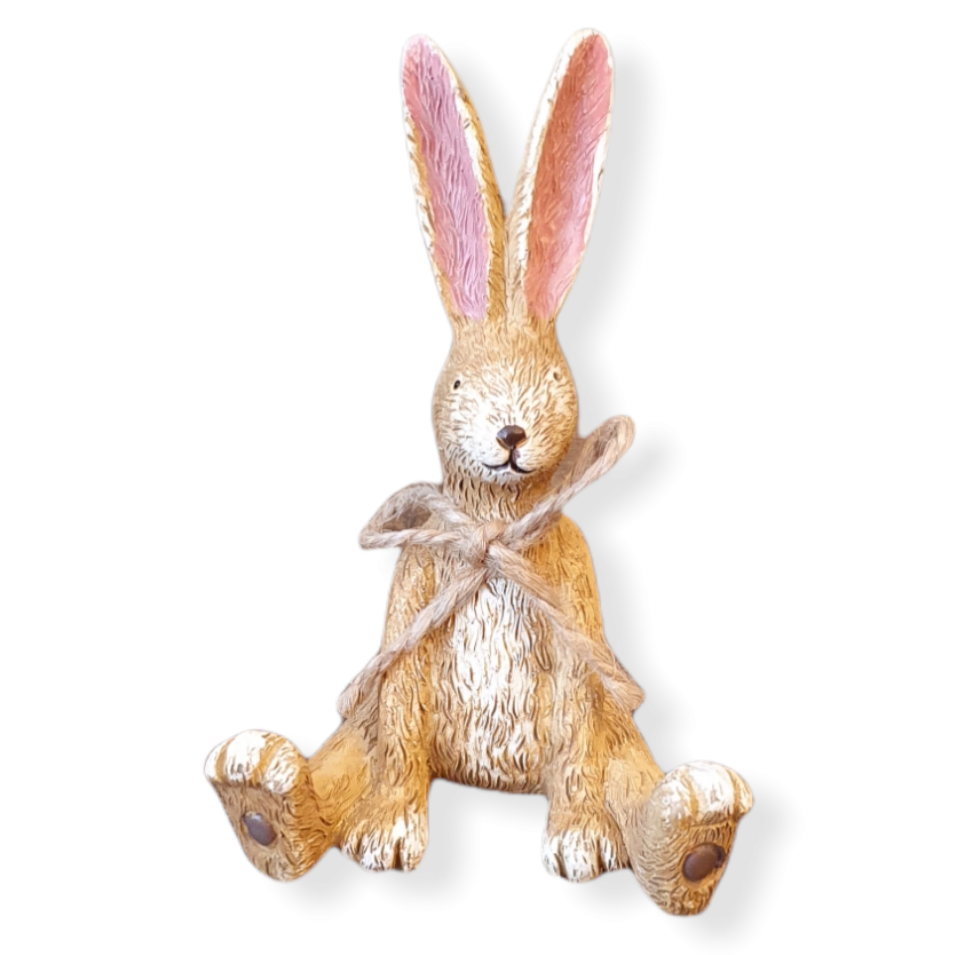 Sitting light brown rabbit, back legs wide apart, front legs inside. Cream chest, face and toes, fur markings all over, tall pink ears and a jute string bow around neck.