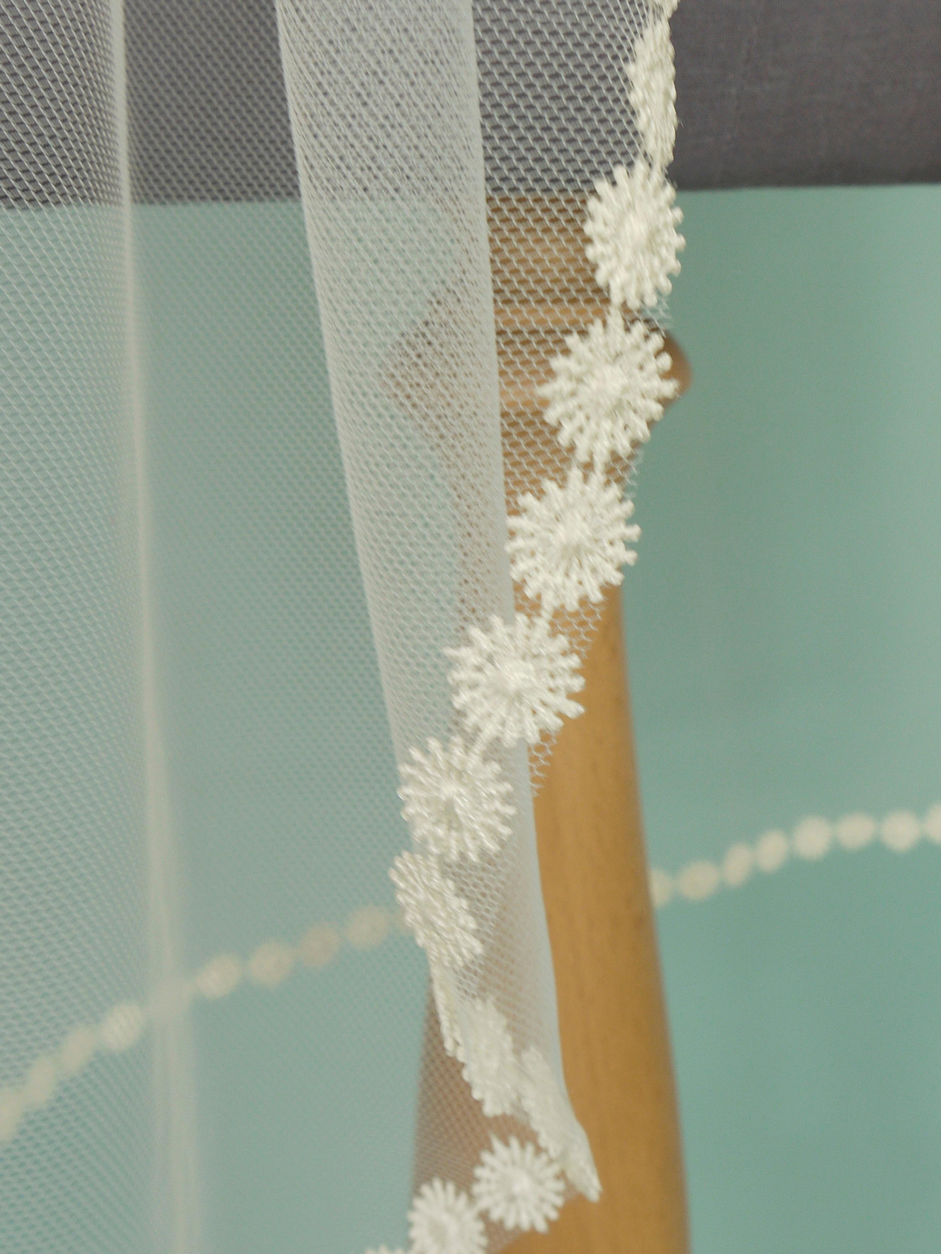 Ivory coloured wedding veil with a floral trim on the bottom edge