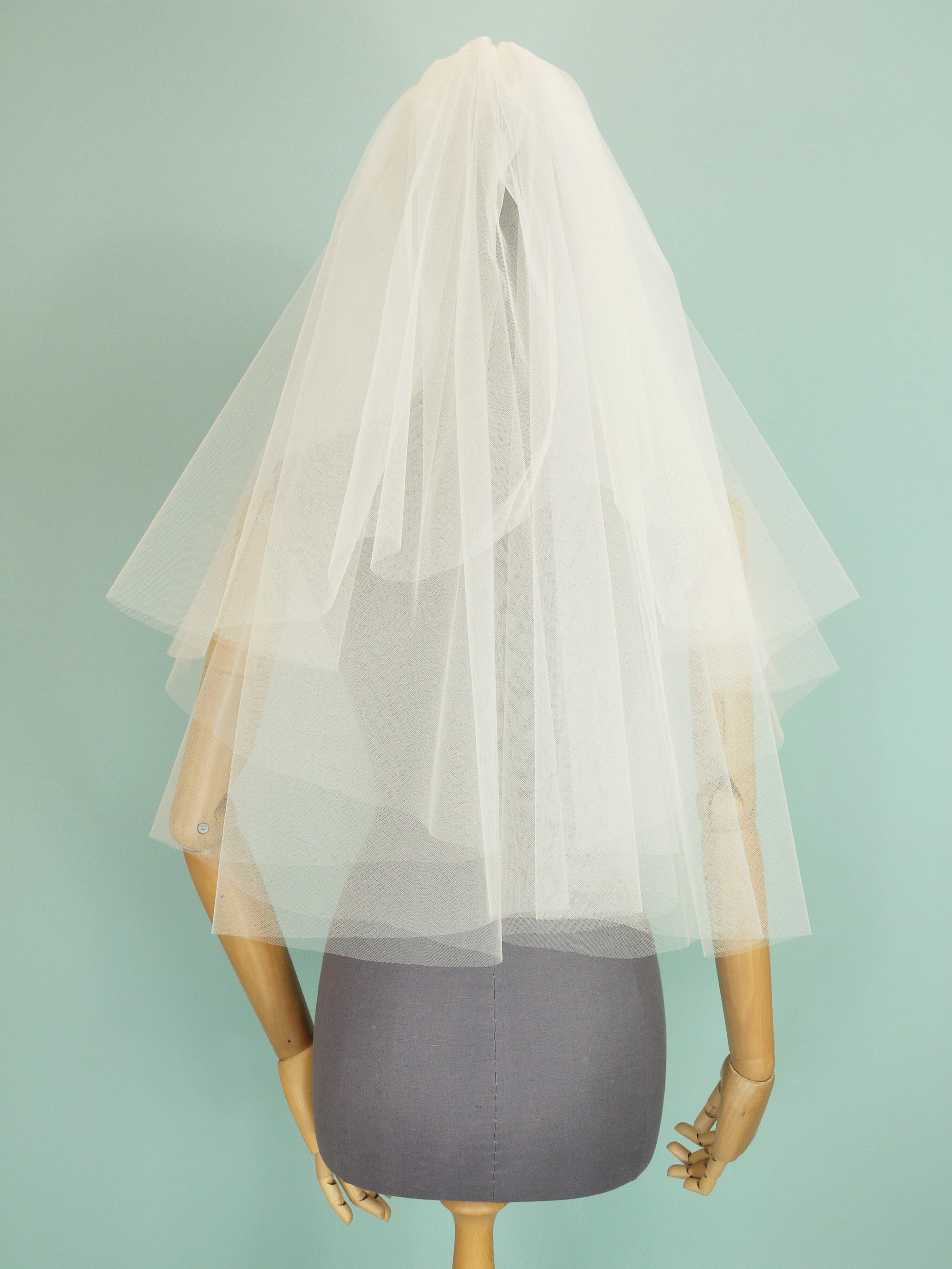 An ivory tulle wedding veil with a tiered shape on a grey mannequin