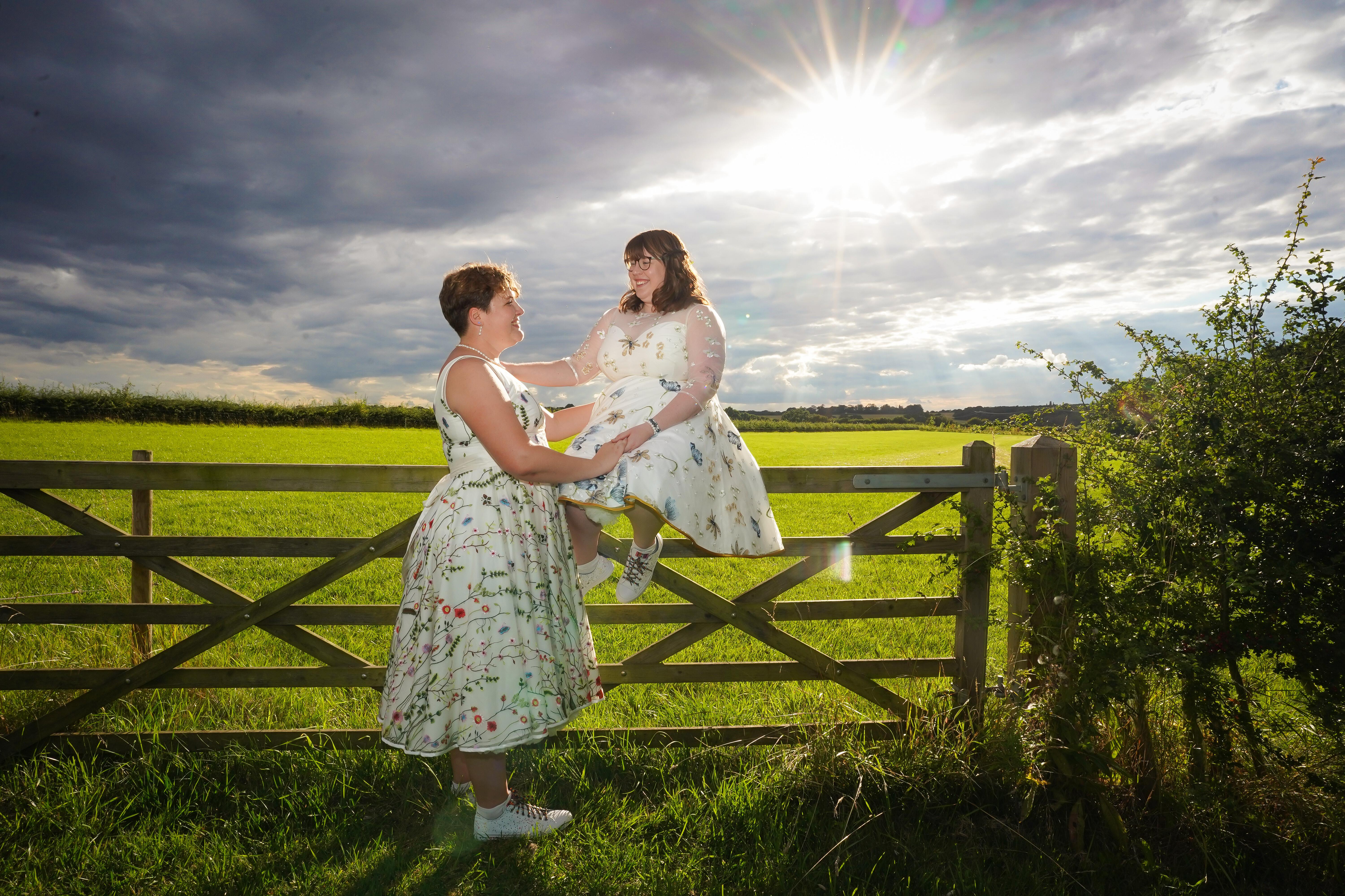 Two beautiful plus size brides in a sunlit field wearing custom Dig For Victory colourful lace wedding dresses