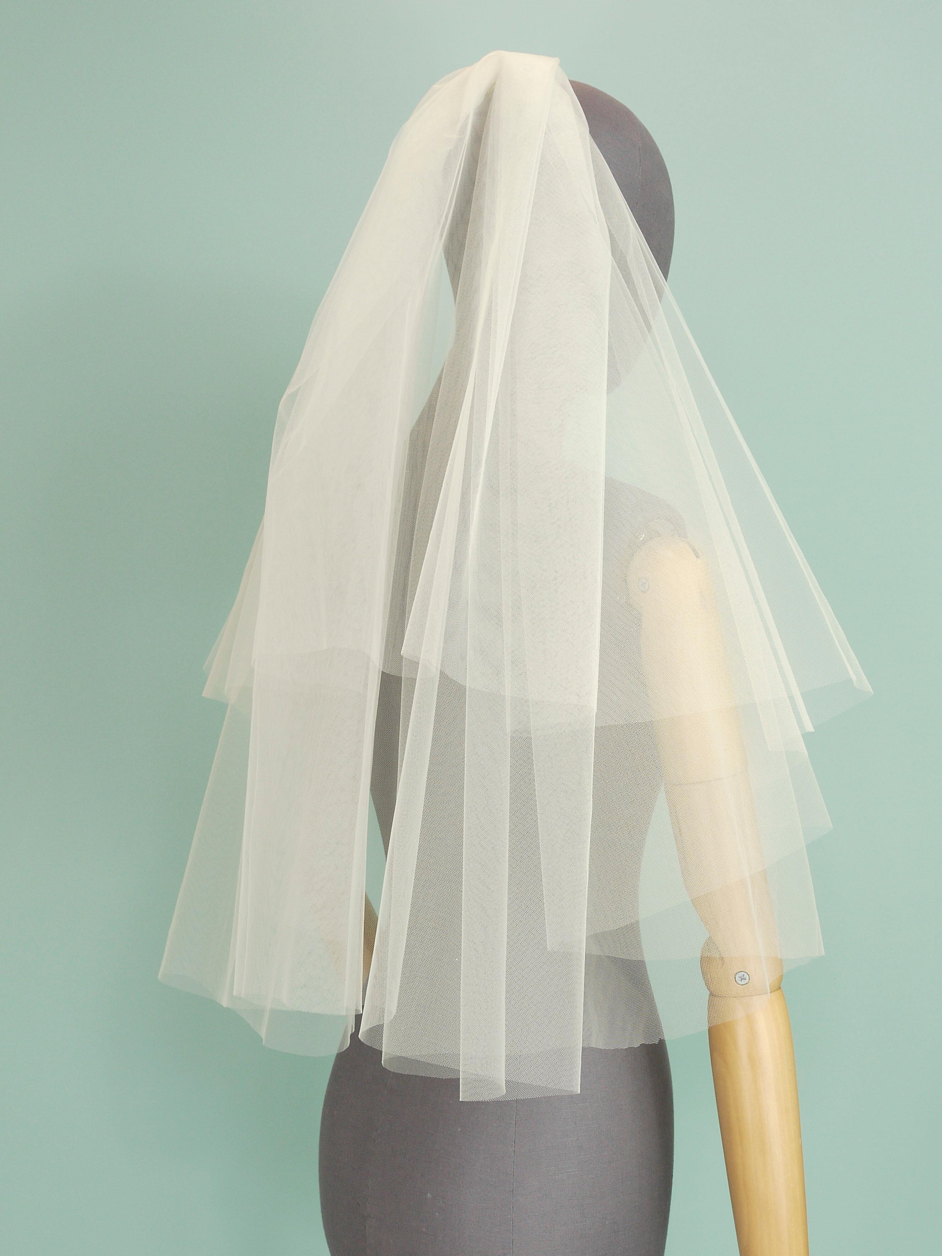 An ivory tulle wedding veil with a tiered shape on a grey mannequin