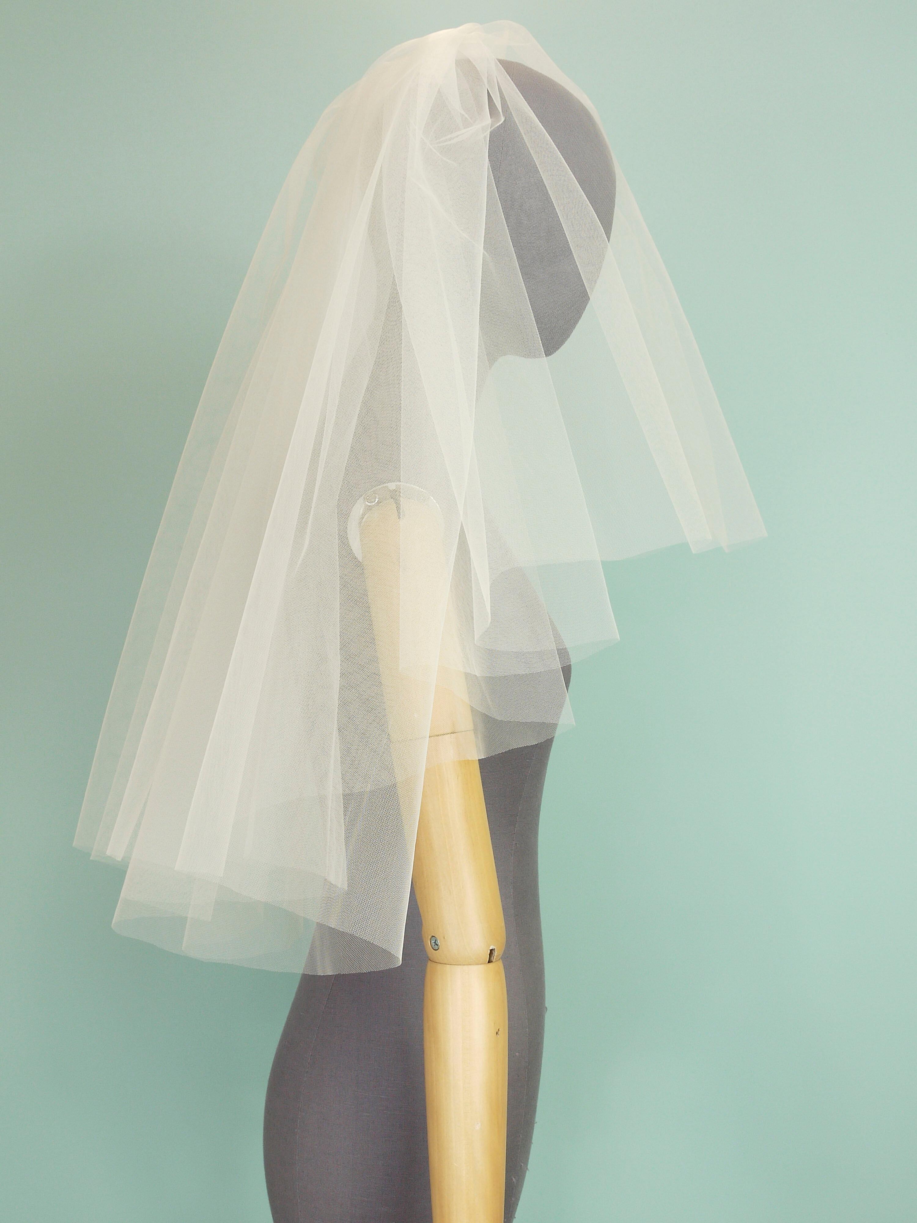 An ivory tulle wedding veil with a tiered shape on a grey mannequin