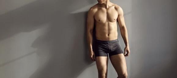 Male model wearing plain grey boxer shorts standing against a dark grey background