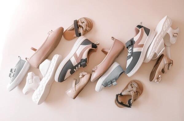 Assorted kids’ trainers in various colors and styles laying on their side on a light pink background.