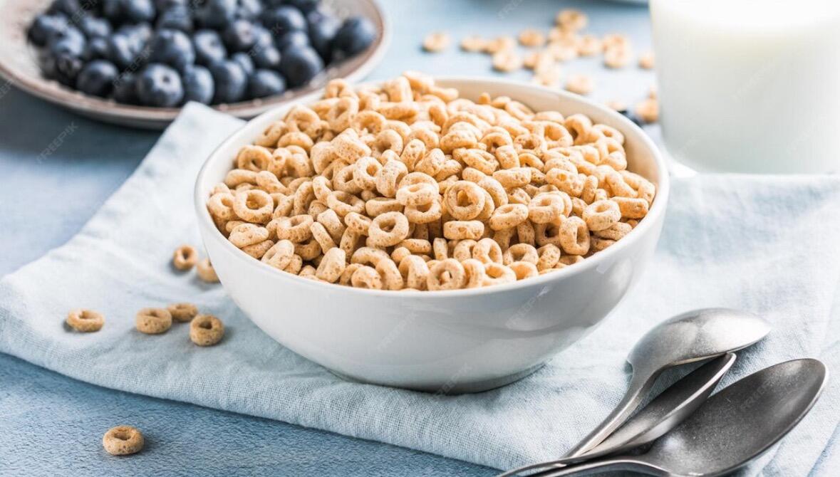 Bowl of fresh blueberries next to a bowl of cereal on a breakfast table.