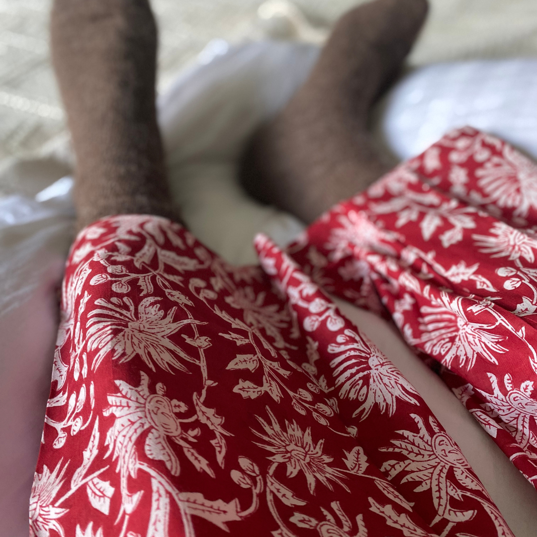 A pair of legs, lying in white sheets, wearing red and white cotton pajama pants, and wooly socks