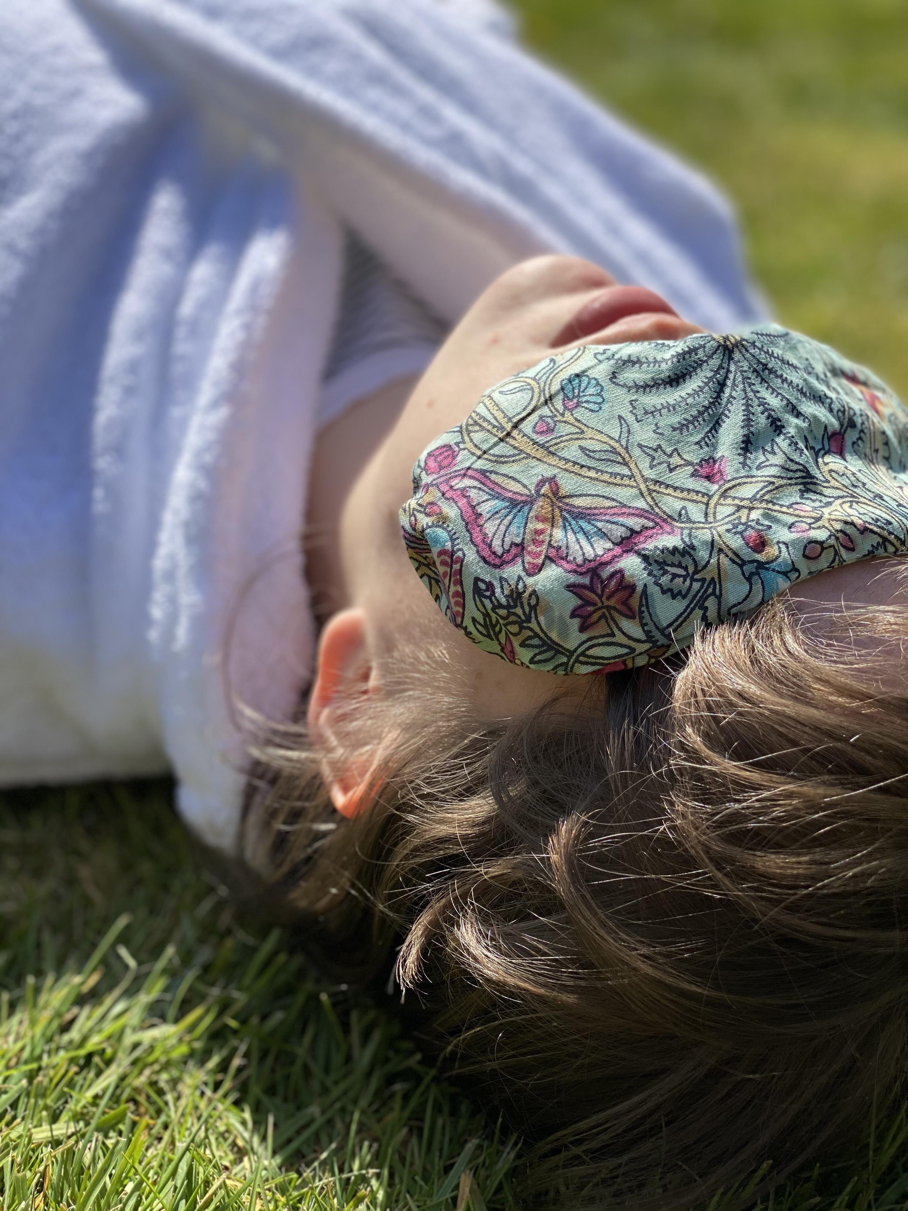 Girl lying on the grass, wearing a lavender eye pillow